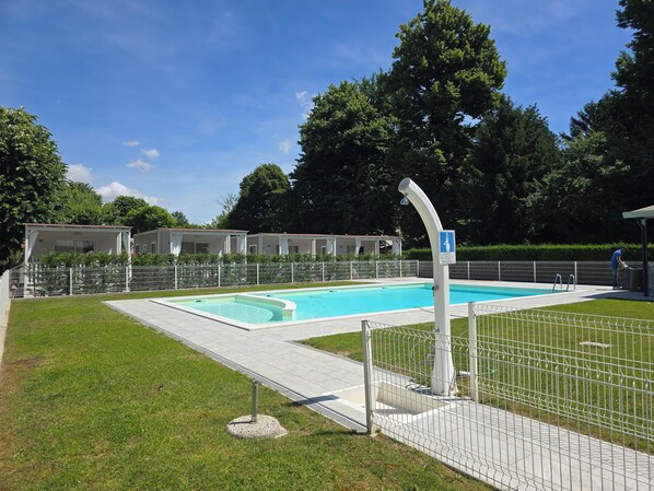 Una piscina con área delimitada por una cerca, un puesto de socorrista y un edificio con porche cubierto al fondo.