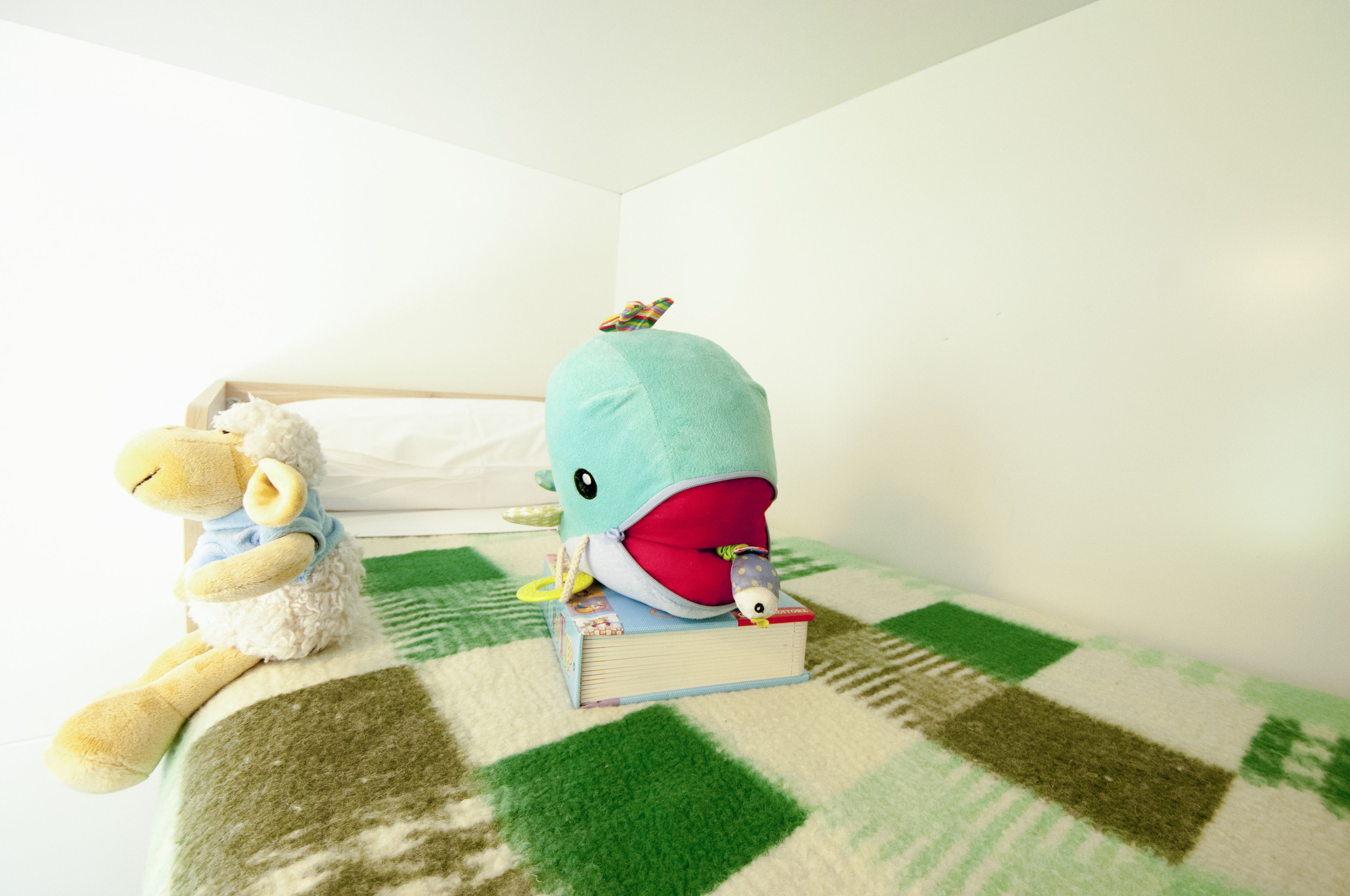 A bed with a checkered green and white blanket, a stuffed whale toy, and a teddy bear.