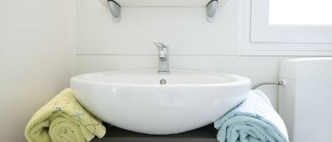 Ein Badezimmer mit einem weißen Waschbecken, einem dunklen Schrank und einem Fenster.