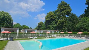 A swimming pool with lounge chairs and umbrellas, surrounded by a fence and greenery. - Camping Serenissima (Mestre)