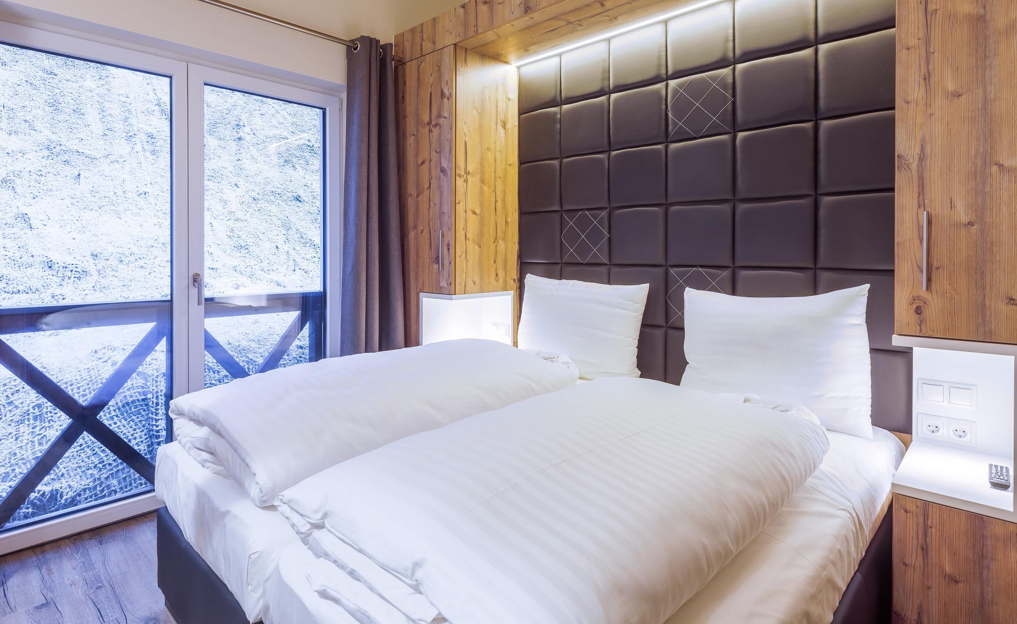A bed with white linens in a room with wooden paneling and a large window.