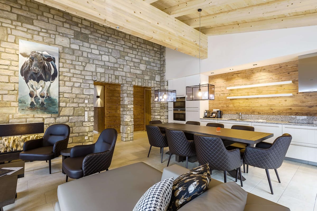Une cuisine moderne aux murs en pierre, un coin repas avec des chaises noires et un grand tableau représentant une vache.