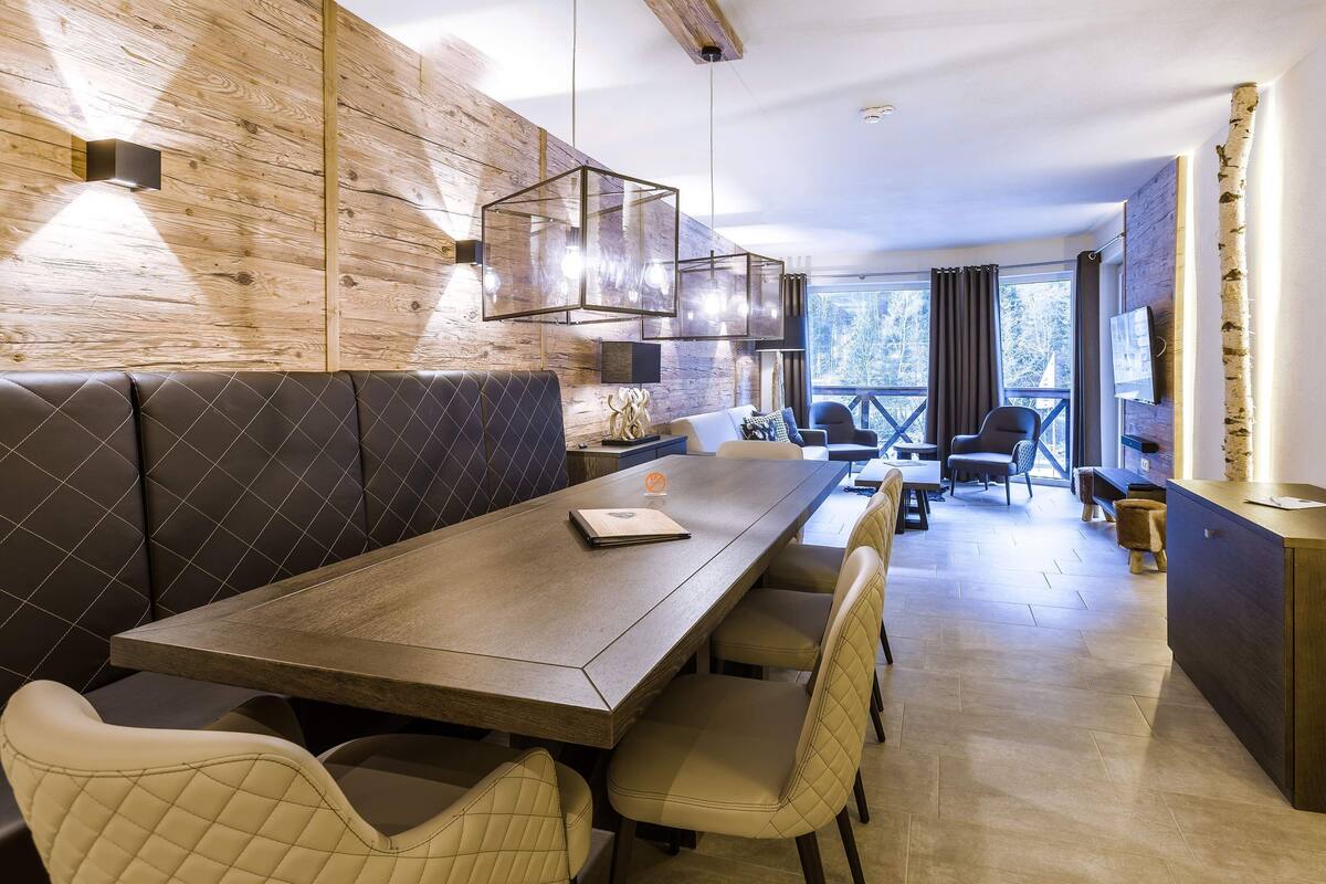 Un espace de restauration moderne avec une longue table en bois, des sièges rembourrés et des luminaires suspendus.