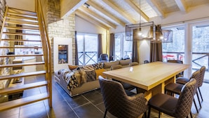 A cozy interior with a wooden staircase, a stone wall, a fireplace, a sofa, a dining table, and chairs.