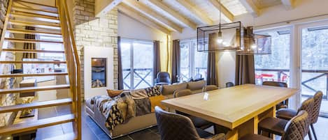 Un interior acogedor con una escalera de madera, una pared de piedra, una chimenea, un sofá, una mesa de comedor y sillas.