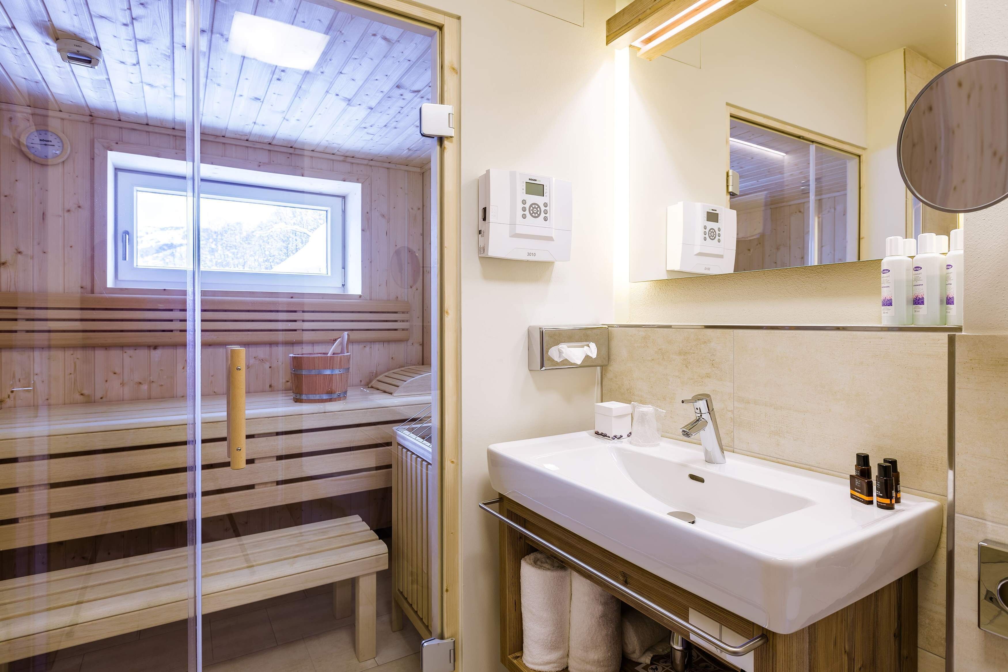 Een moderne badkamer met een houten sauna, een groot wastafel en een spiegel.