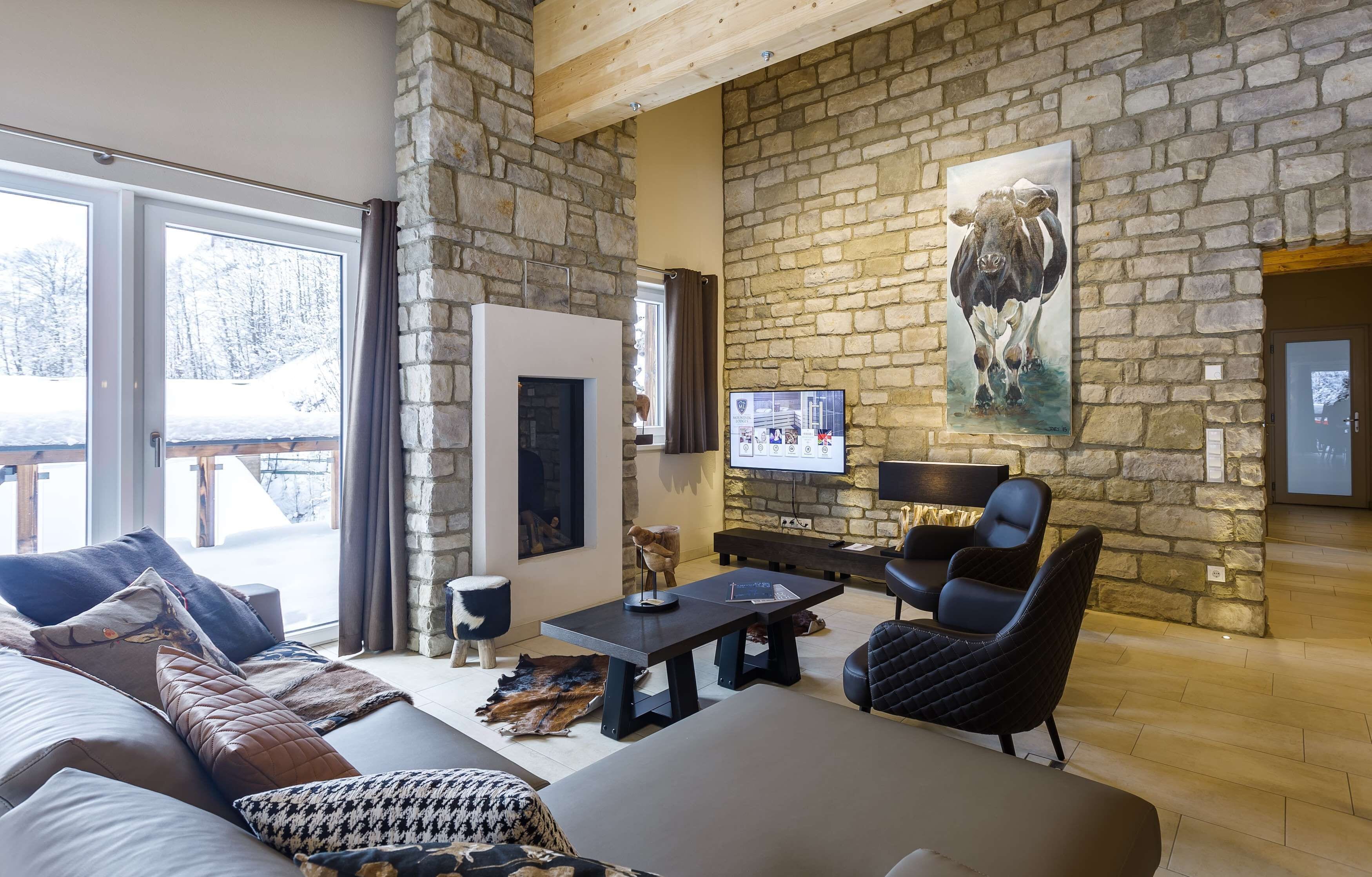 A cozy living room with a stone wall, a fireplace, a television, and comfortable seating.
