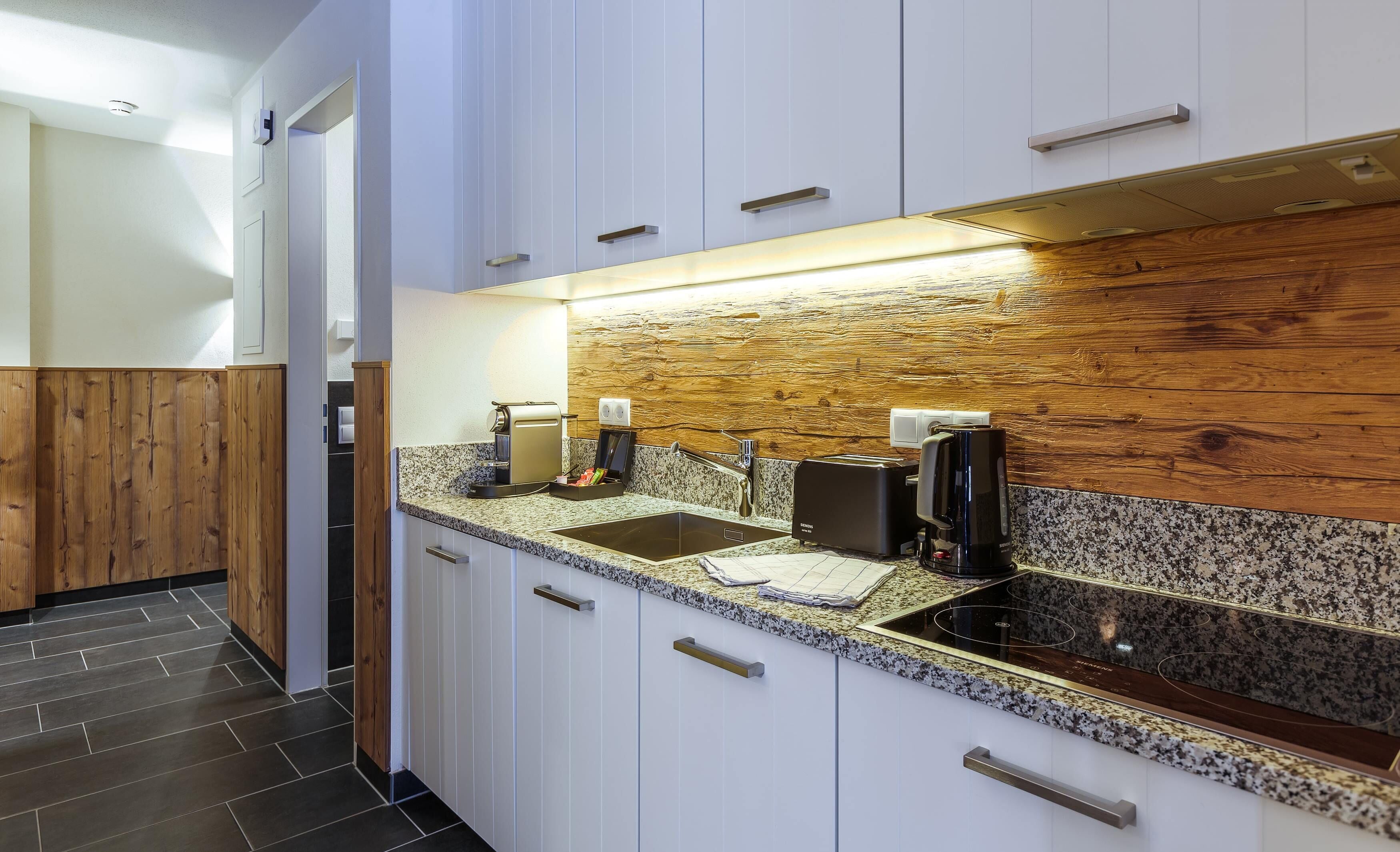 Una cocina moderna con armarios blancos, encimeras de granito, estufa integrada y un salpicadero de madera.