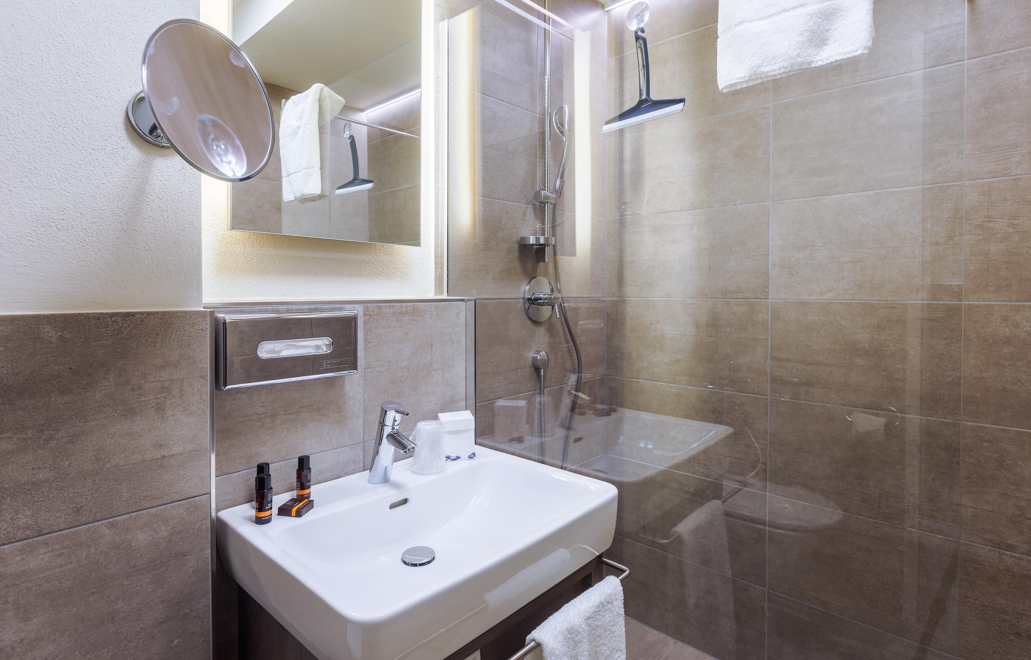 A modern bathroom with a white sink, mirror, and shower.