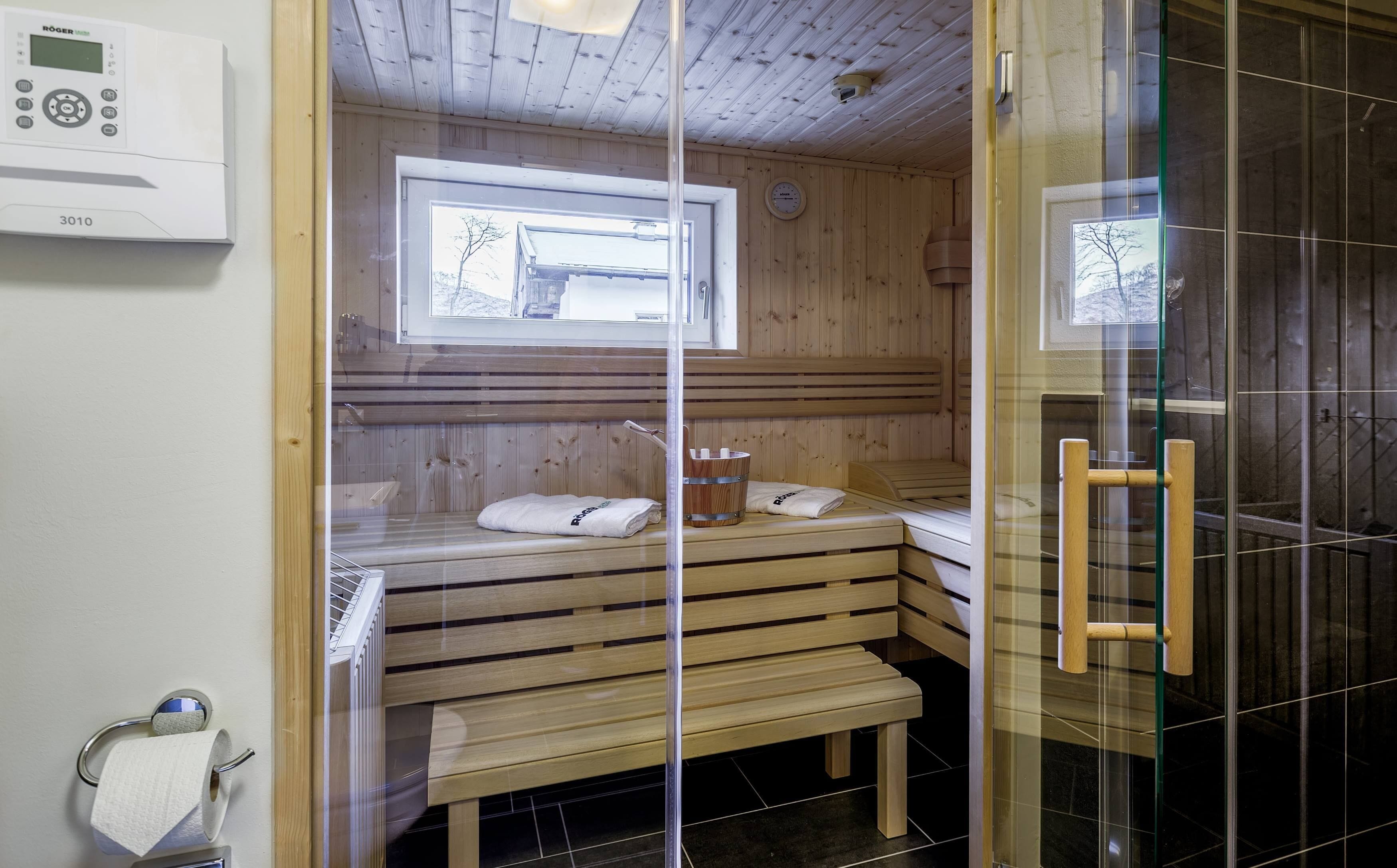 A sauna with wooden benches, a window, and a control panel on the wall.