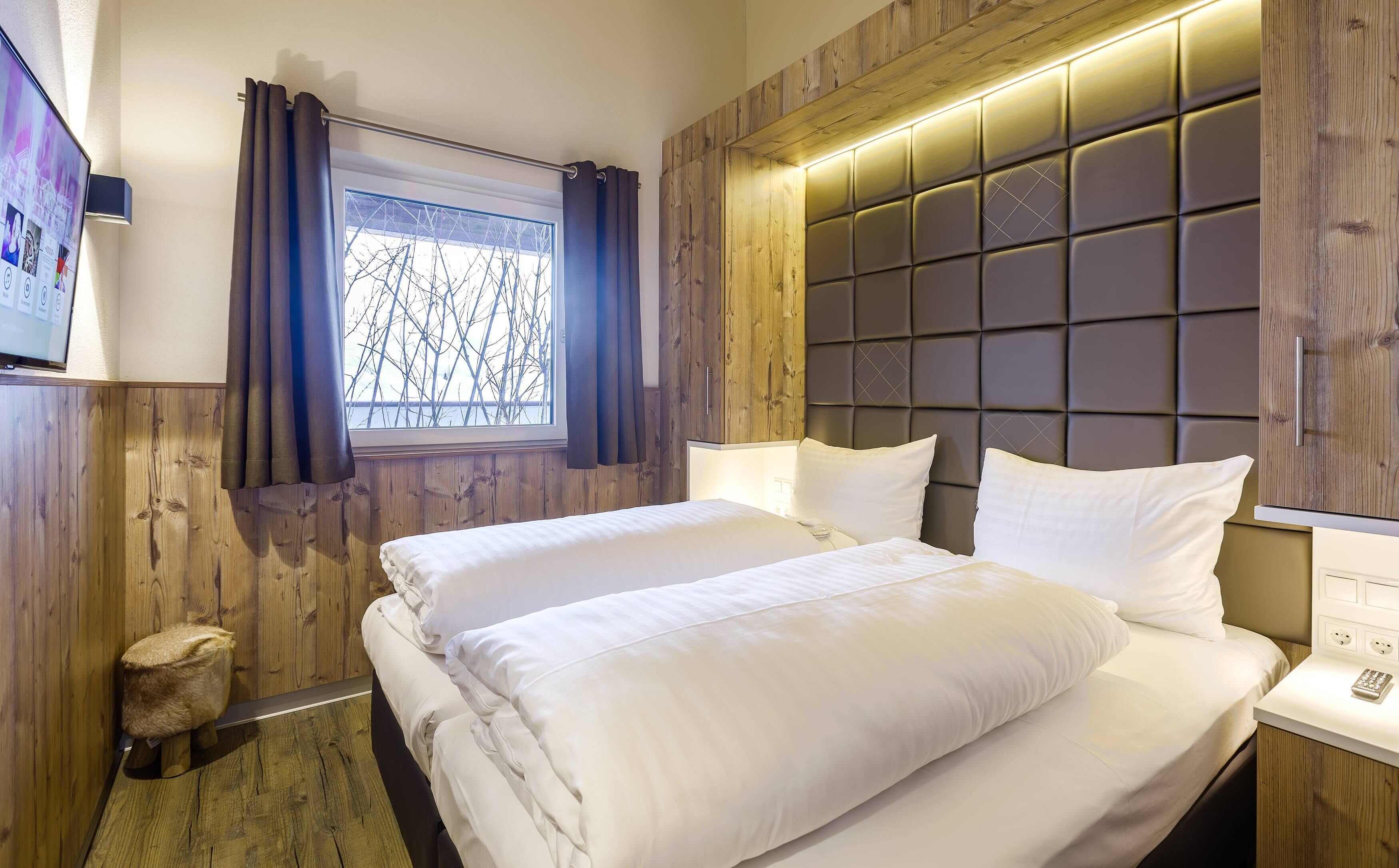 A hotel room with a large bed, wooden paneling, a window with curtains, and a modern headboard.