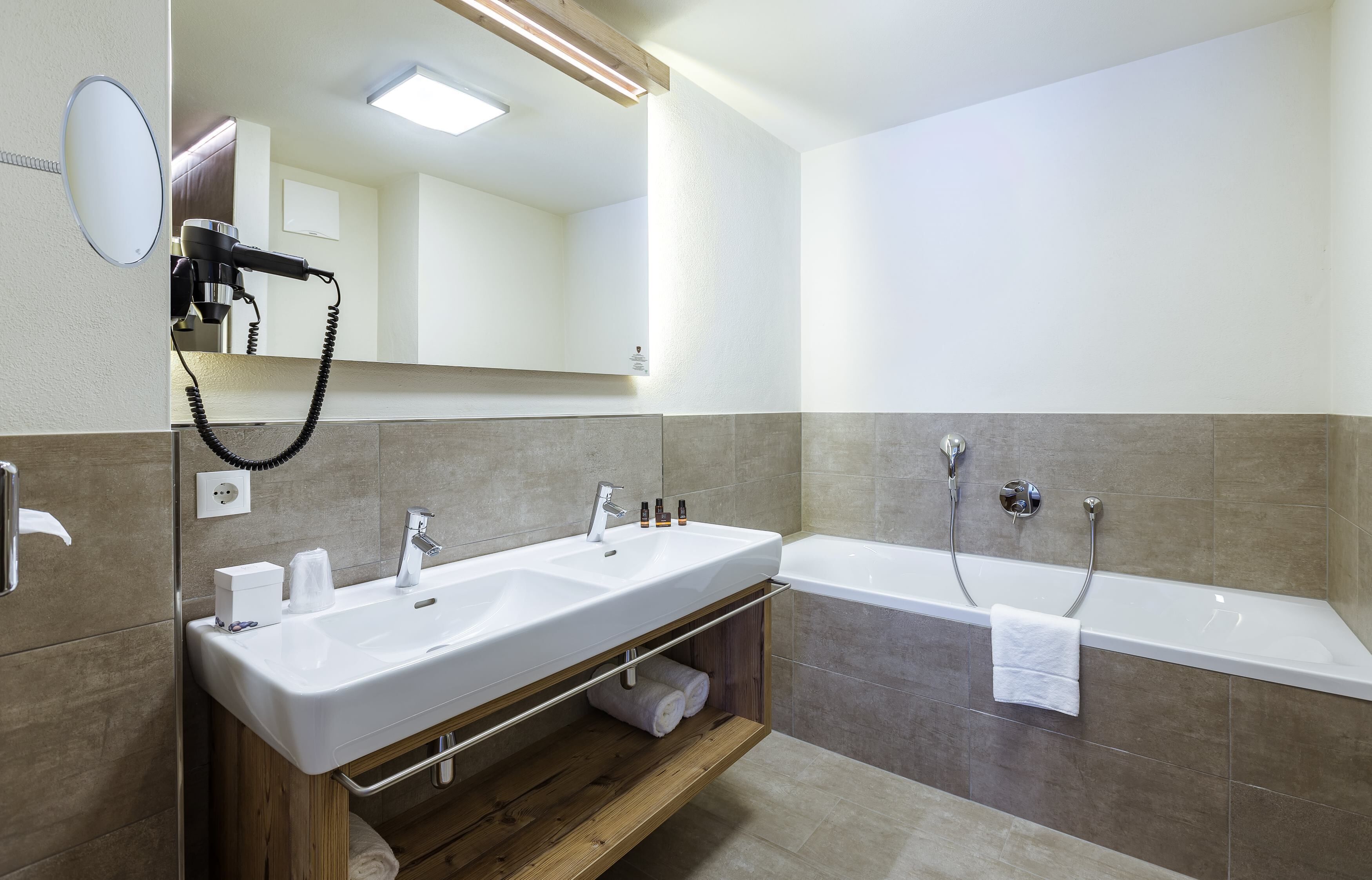 A modern bathroom with a double sink, a hairdryer, a mirror, and a bathtub.
