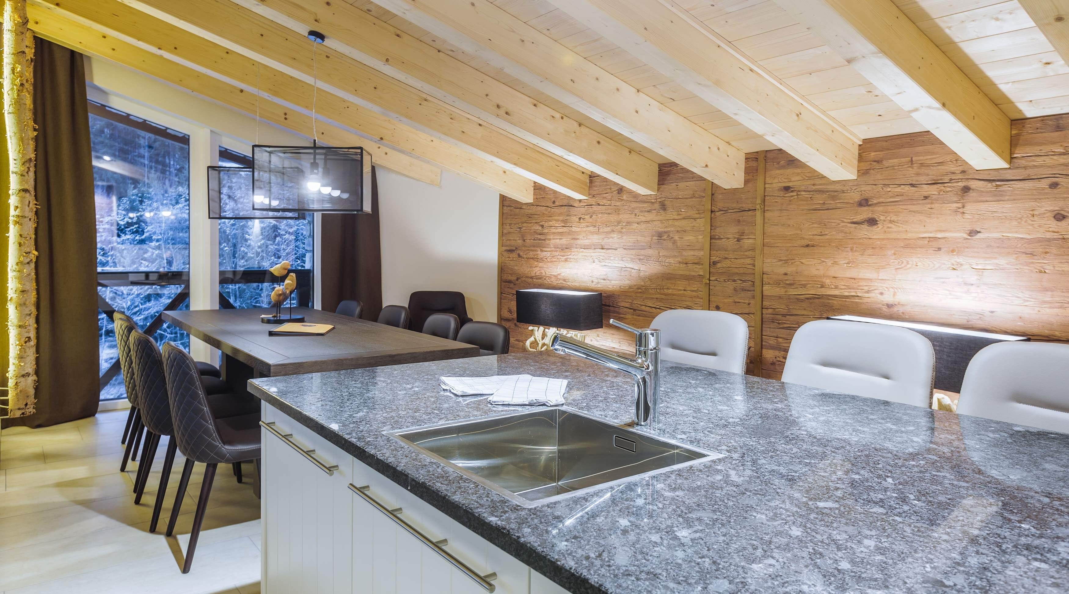 A modern kitchen with a granite countertop, stainless steel sink, and wooden ceiling beams.