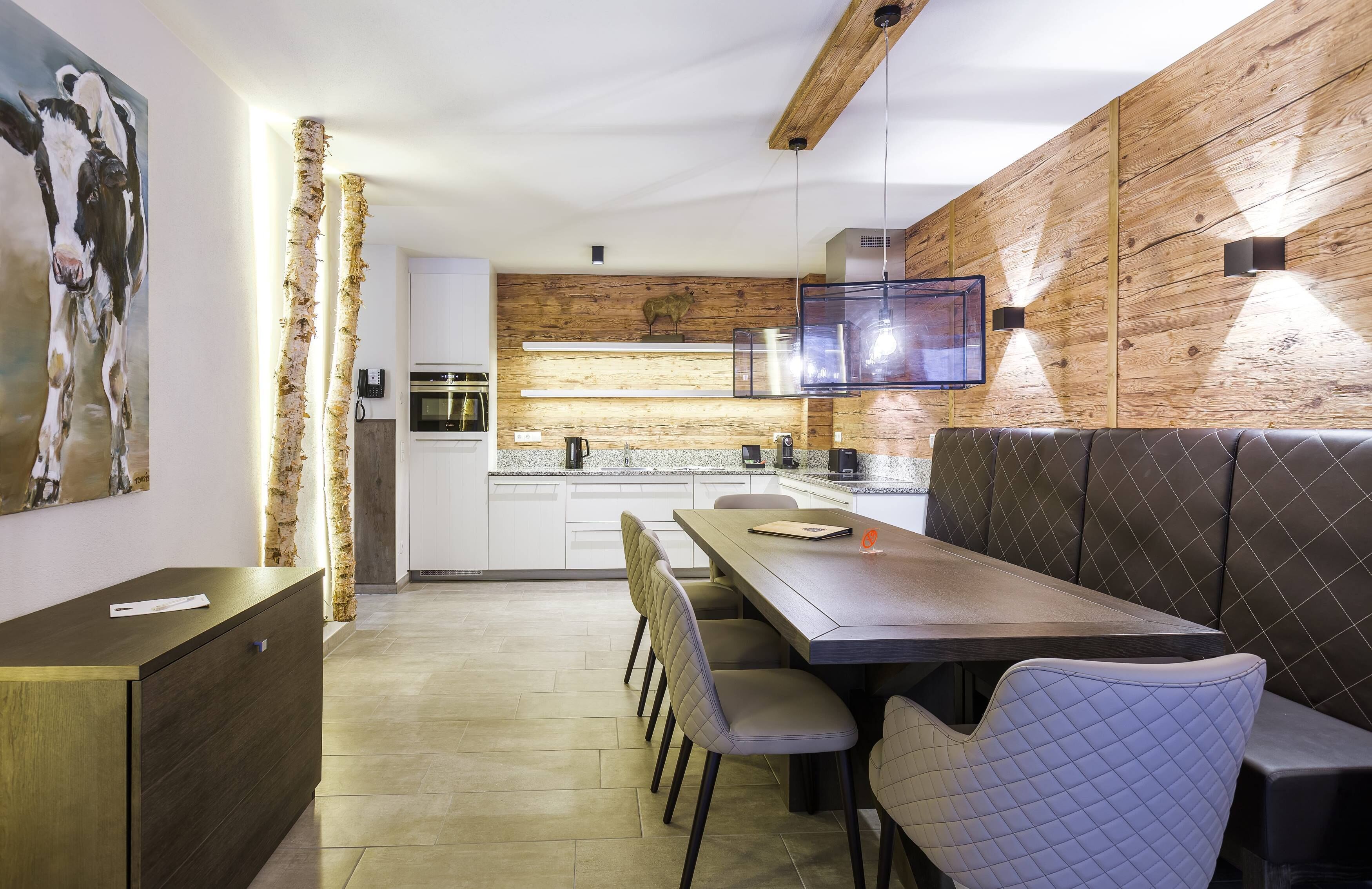 A modern kitchen with wooden accents, a dining area with cushioned seating, and a large painting on the wall.