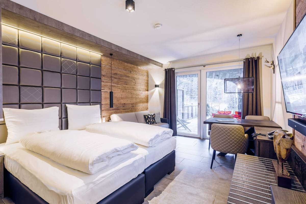 Une chambre d’hôtel moderne dotée d’un grand lit, d’une tête de lit en bois, d’un bureau avec une chaise et offrant une vue sur l’extérieur.