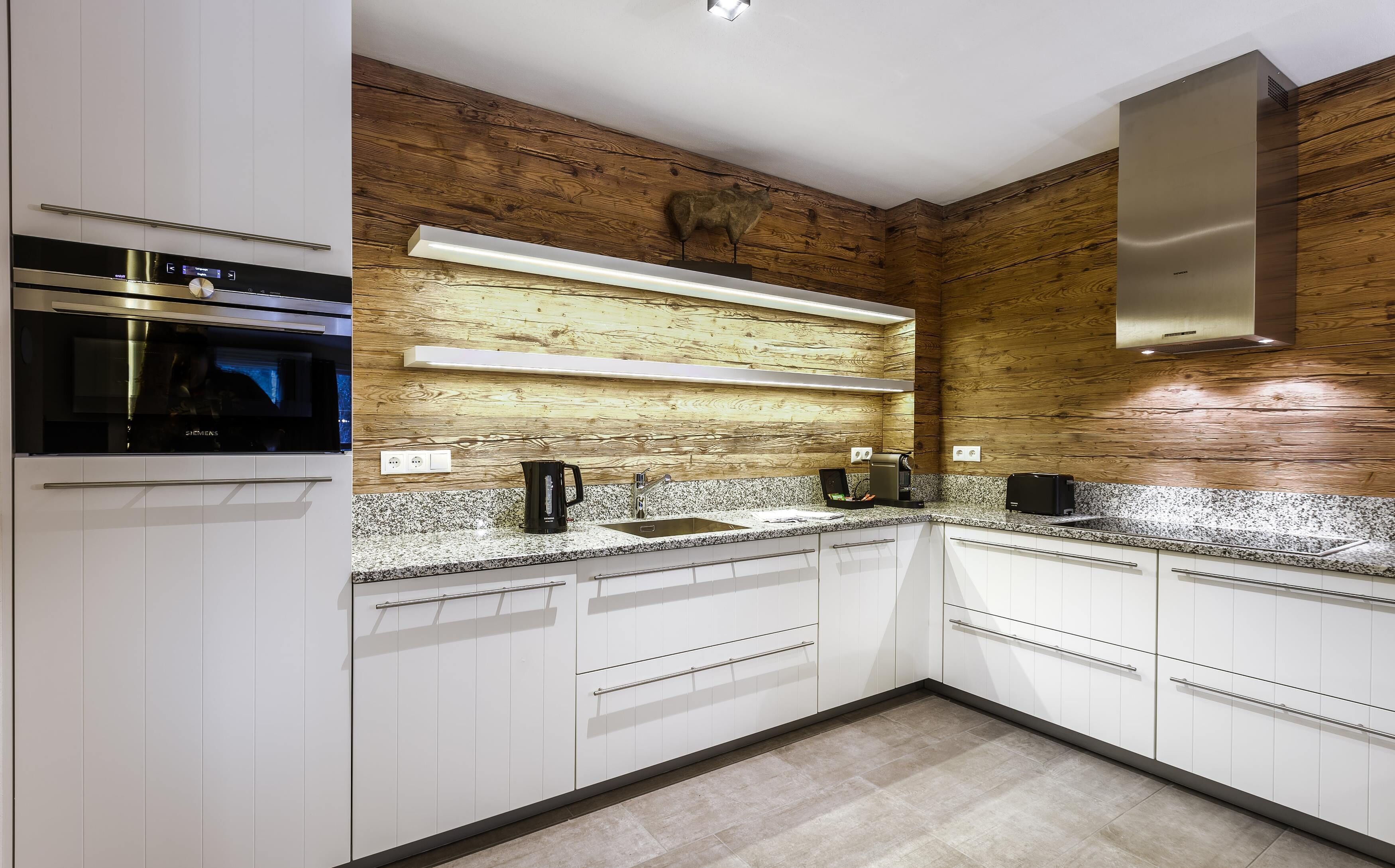 Una cocina moderna con armarios blancos, un revestimiento de pared de madera, un horno empotrado y una campana extractora de acero inoxidable.
