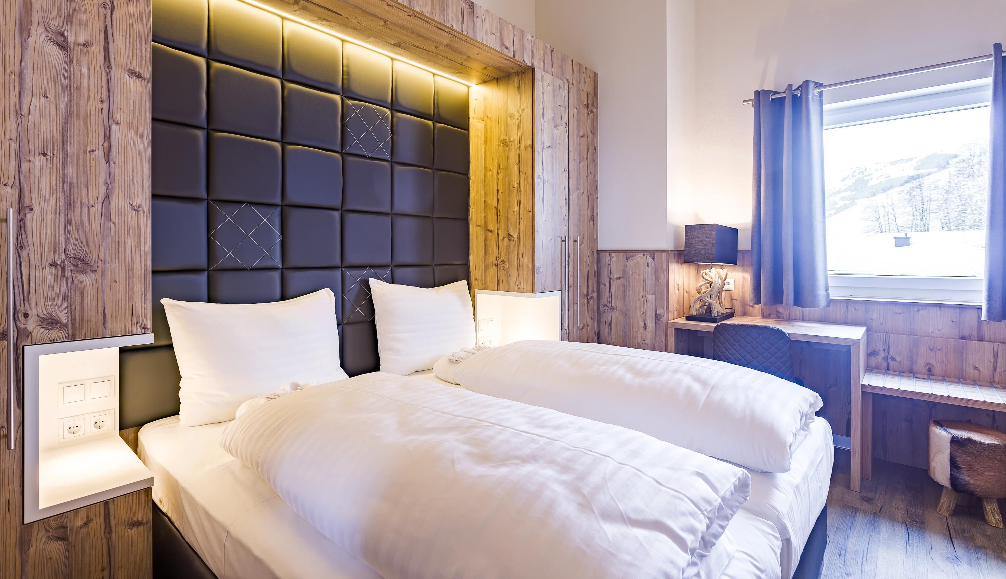A hotel room with a large bed, bedside tables, a desk, and a window with curtains.