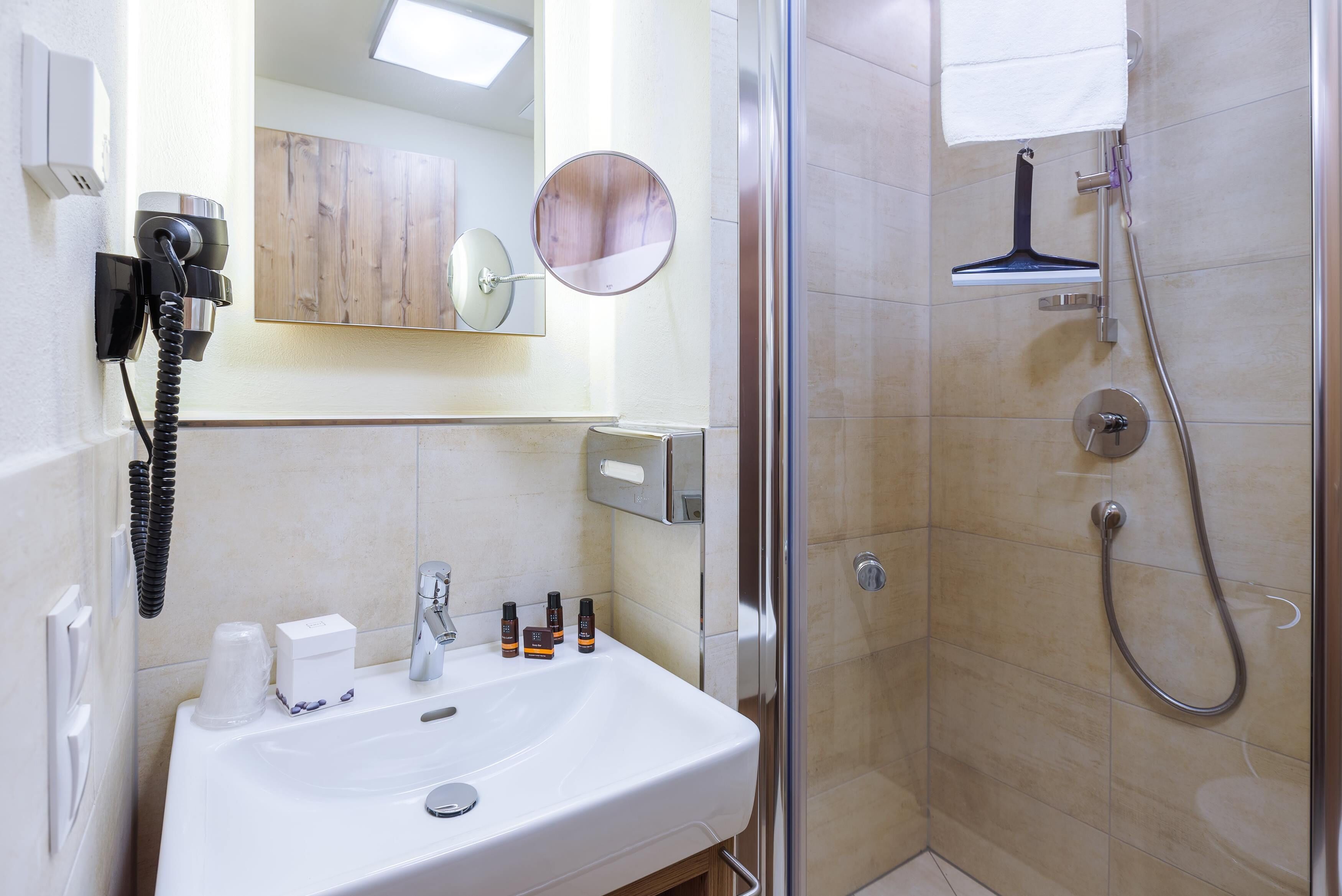 A bathroom with a sink, mirror, hairdryer, and shower.