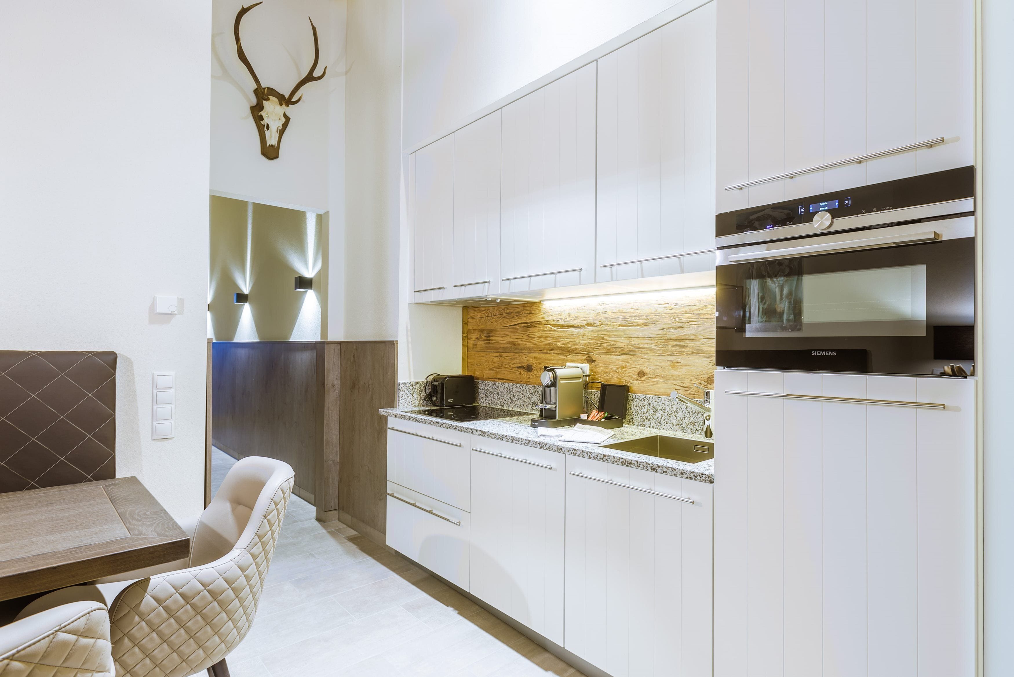 A modern kitchen with white cabinets, a wooden backsplash, and a mounted deer skull.