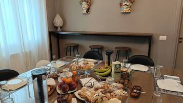 A dining table set with various pastries, fruits, and beverages, with chairs around it.