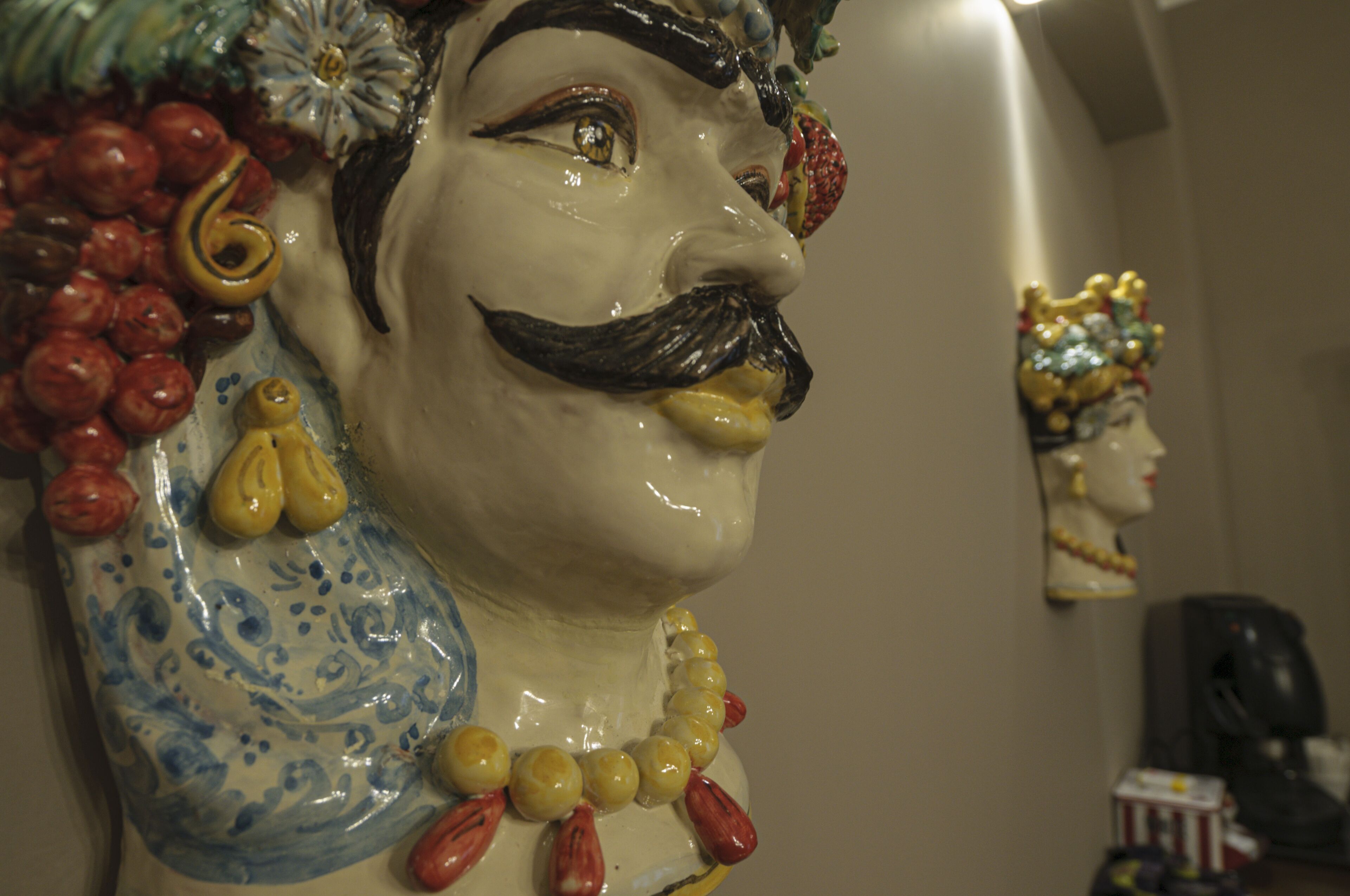 Una scultura in ceramica con baffi e perline, posata su una superficie decorata.