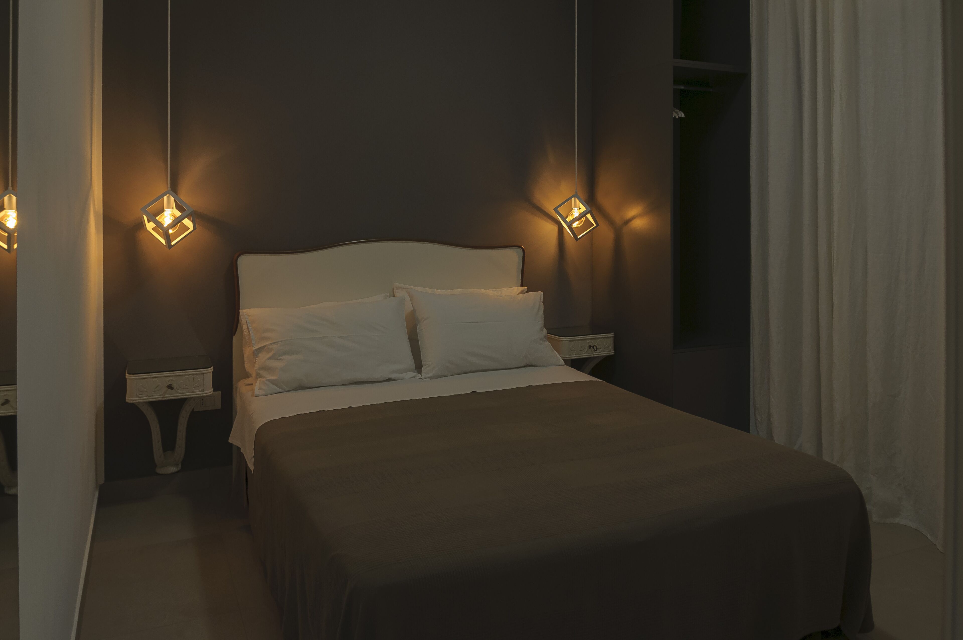Um quarto com uma cama, duas mesas de cabeceira e duas luzes fixadas na parede.