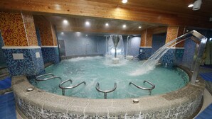 Ein Whirlpool mit Wand aus Mosaikfliesen, Holzboden und Metallgeländern.