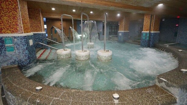 Ein Whirlpool mit zahlreichen Düsen, umgeben von Wandfliesen aus Mosaik und Holzbalken.