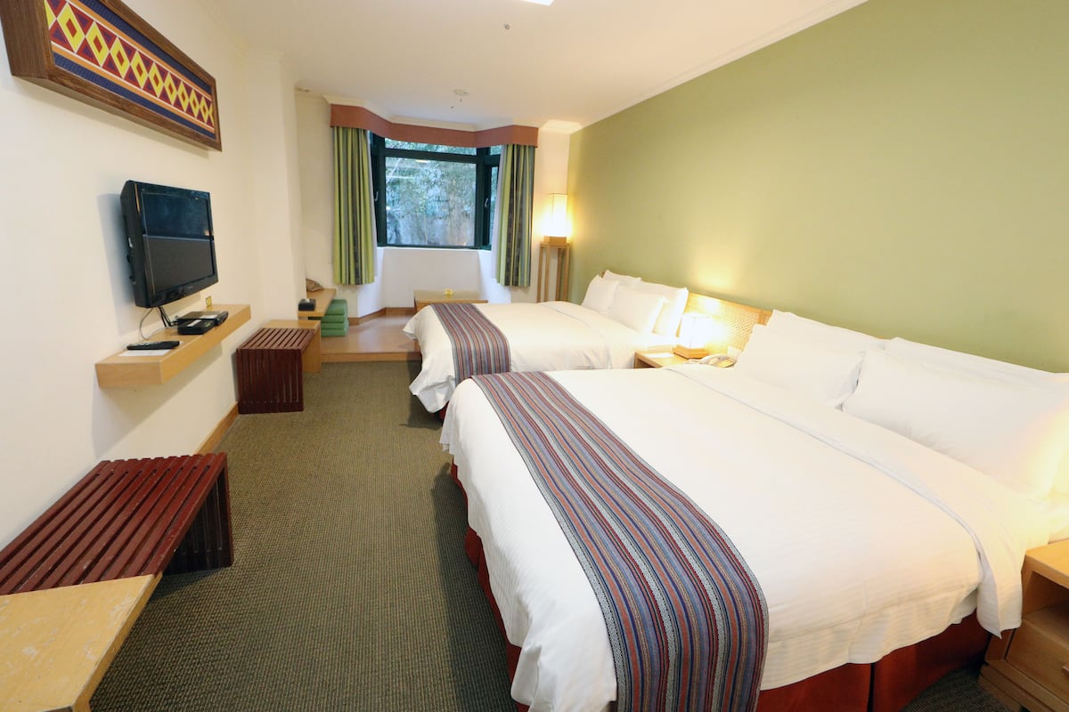 A hotel room with two beds, a television, a desk, and a window with curtains.