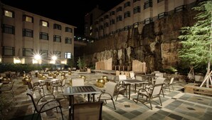 Eine Außenpatio-Terrasse mit Tischen und Stühlen, einer Felswand und einem Gebäude im Hintergrund.