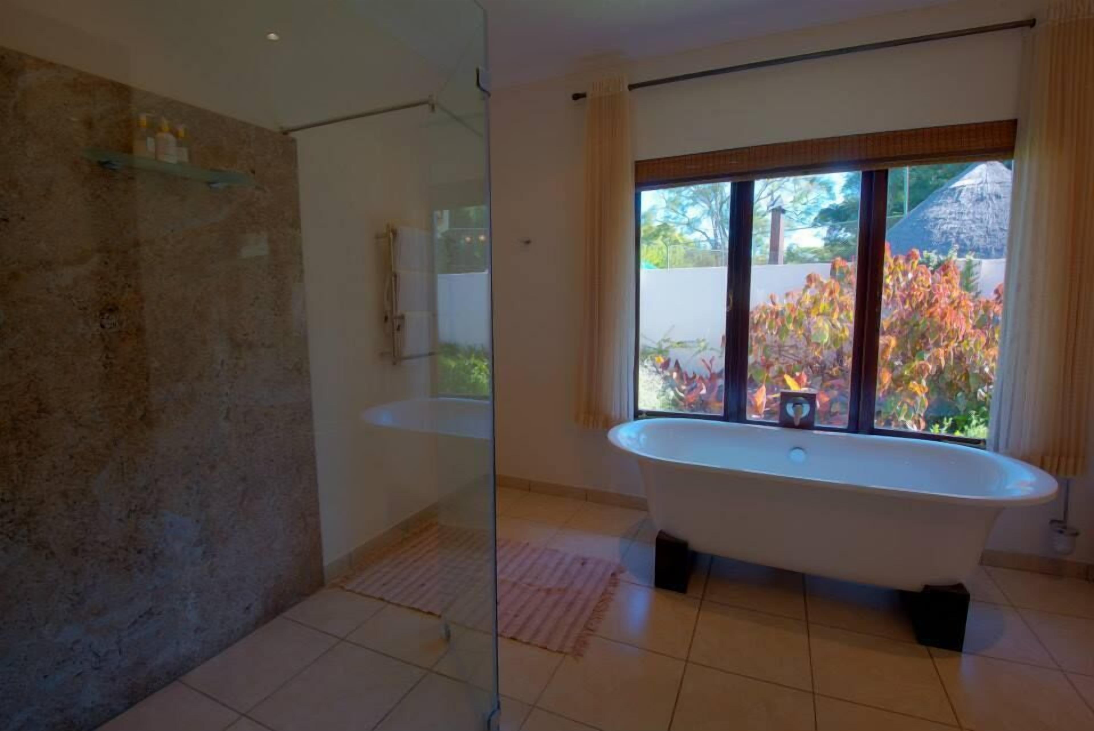 A modern bathroom with a freestanding bathtub, a glass shower enclosure, and a large window offering a view of the outdoors.