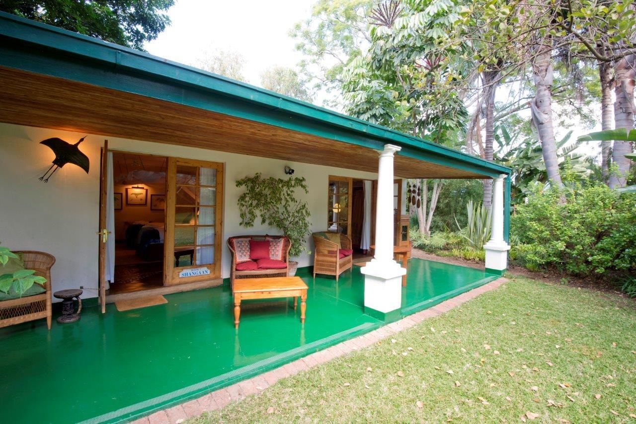 Una casa con techo verde, un porche cubierto con muebles y un jardín.