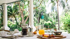 A breakfast setup with a coffee pot, teapot, and jug of orange juice on a table, surrounded by greenery. - York Lodge (Harare)