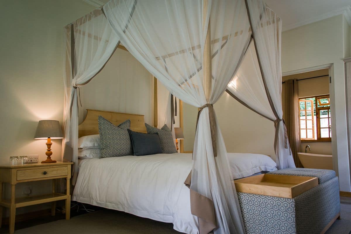 A four-poster canopy bed with a wooden headboard, bedside tables, and a small wooden bench.