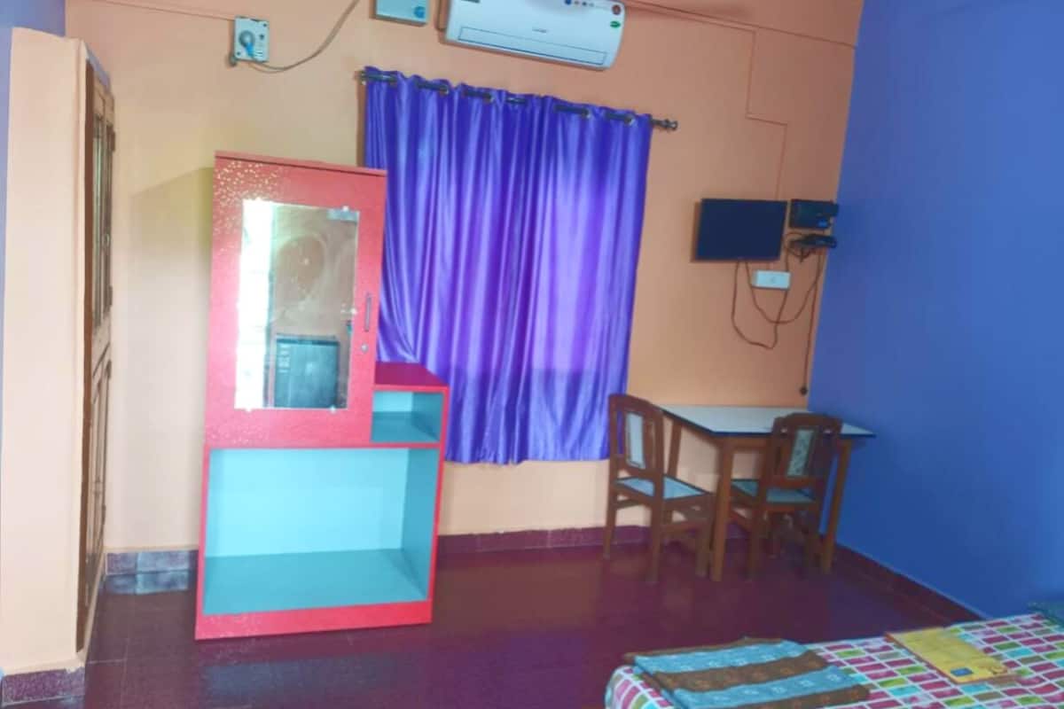 A room with a bed, a desk, a chair, a window with purple curtains, and an air conditioning unit.