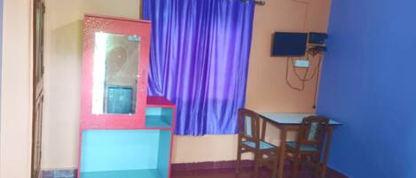 Una habitación con cama, escritorio, silla y ventana con cortinas moradas, además de un equipo de aire acondicionado.
