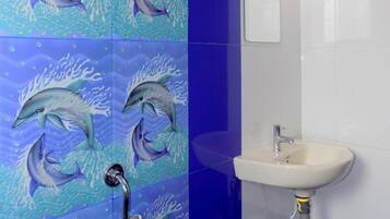 Un baño con un muro de azulejos con motivos de delfines, un lavamanos blanco y un espejo.