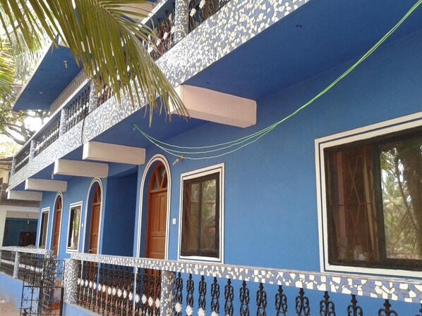 A blue building with arched windows and a balcony with a patterned railing.