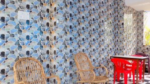 A room with a mosaic wall, two wicker chairs, a red table, and a checkered floor.