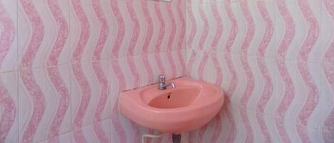 A bathroom with pink and white patterned tiles, a pink sink, and a mirror.