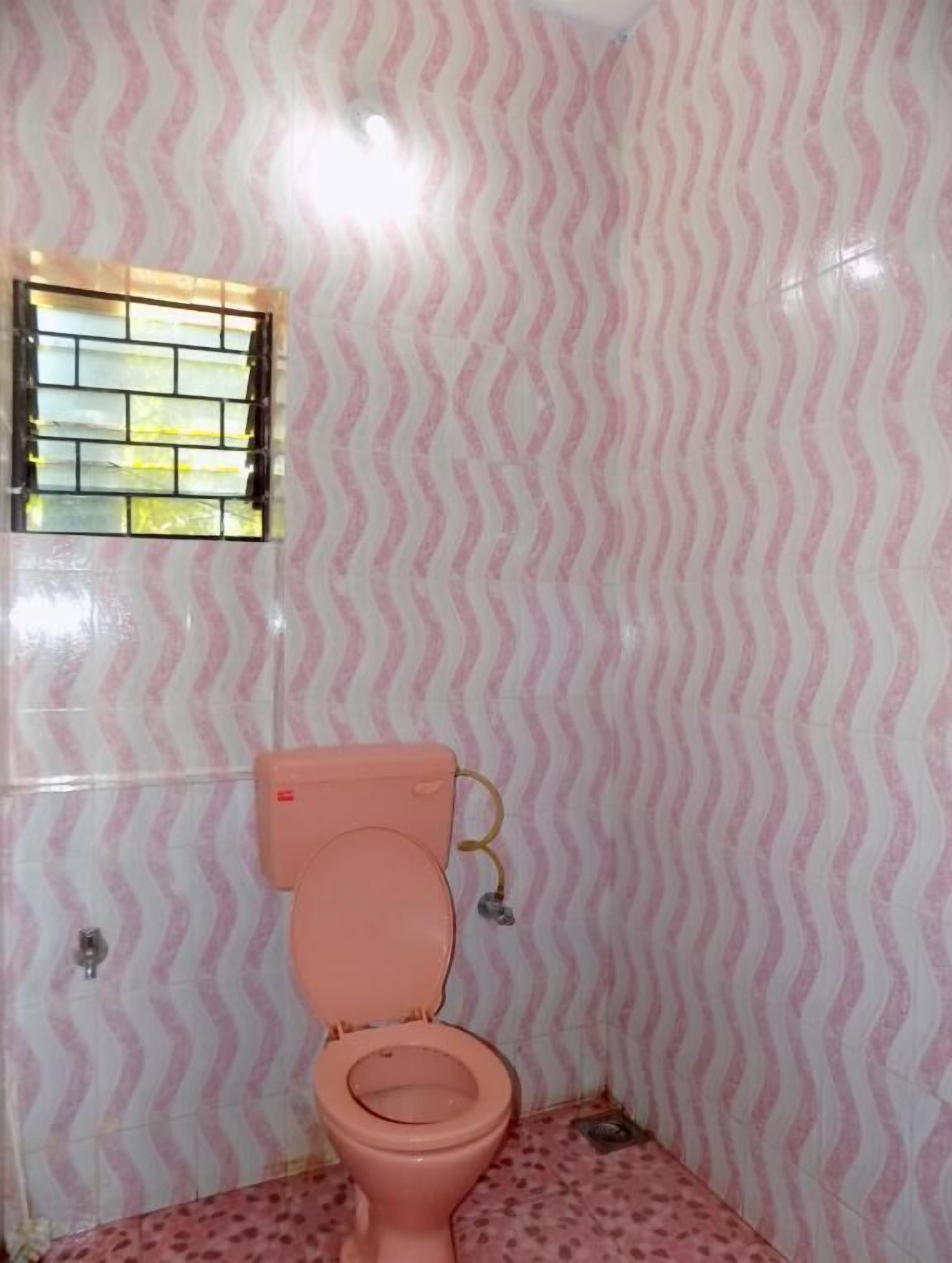 A bathroom with a pink patterned wall, a pink toilet, and a window with a metal grate.