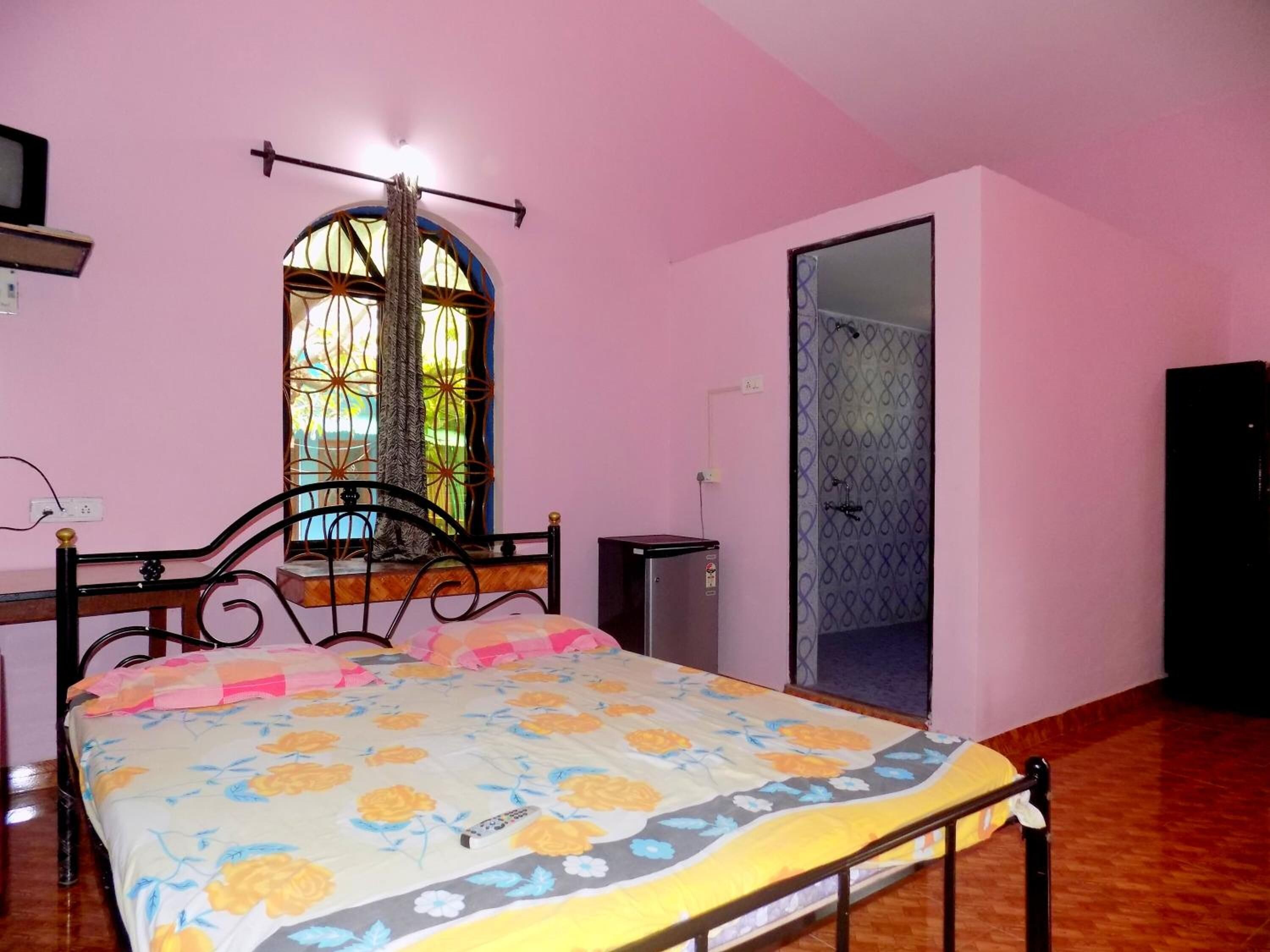 A bedroom with a bed, a window with a curtain, a mirror, and a door.