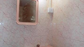 A bathroom with a pink sink, a mirror, and a light fixture on the wall.