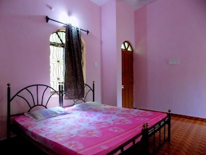 Un dormitorio con cama, ventana con cortinas, puerta y toma de corriente.