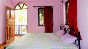 A bedroom with a bed, a window with red curtains, a ceiling fan, and an open door leading outside.