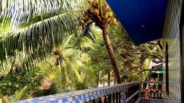 A tiled walkway with a decorative railing, palm trees, and a view of a building with patterned walls.