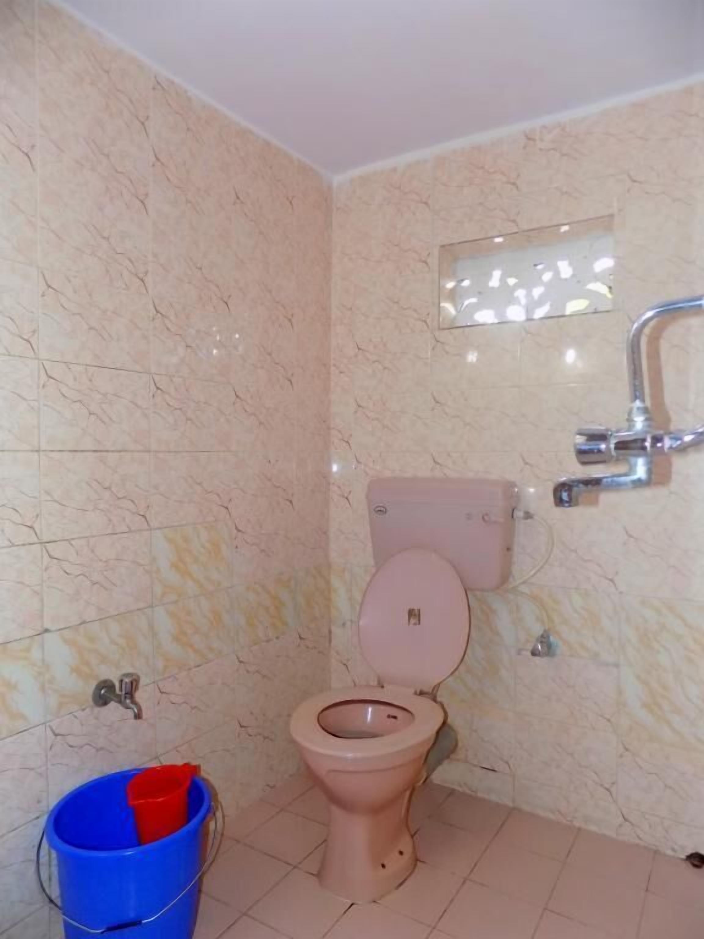 Un baño con inodoro, un cubo azul y un espejo.