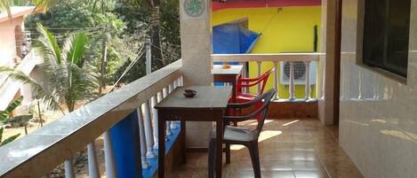 Un balcón con mesa y sillas, piso de baldosas y vista a un edificio amarillo con techo rojo.