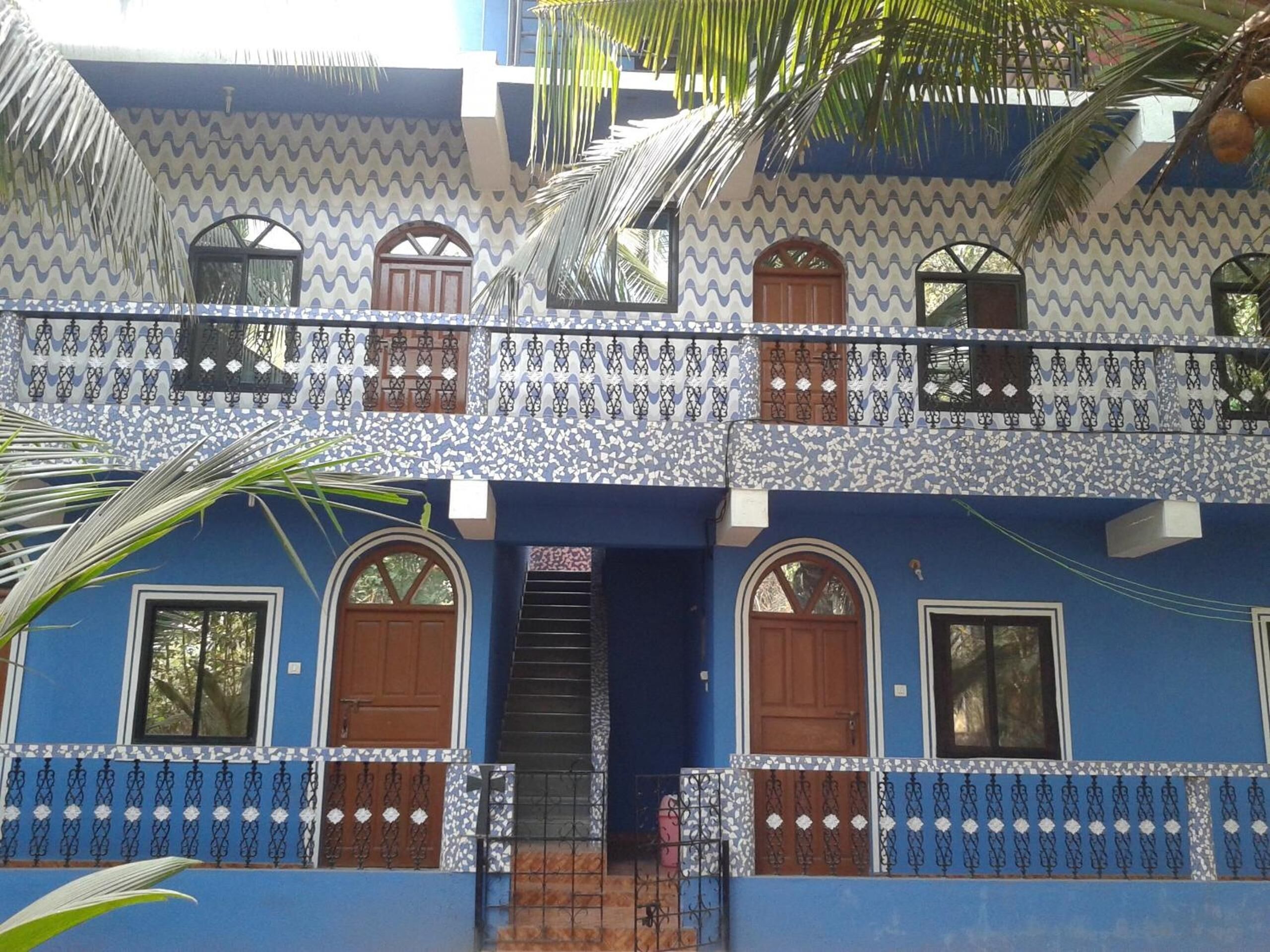 A two-story building with a blue facade, multiple windows with brown doors, and decorative metal railings.