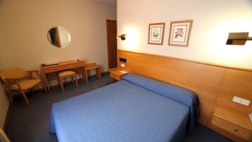 Habitación de hotel con una cama, un escritorio, una silla, un espejo y dos cuadros en la pared.